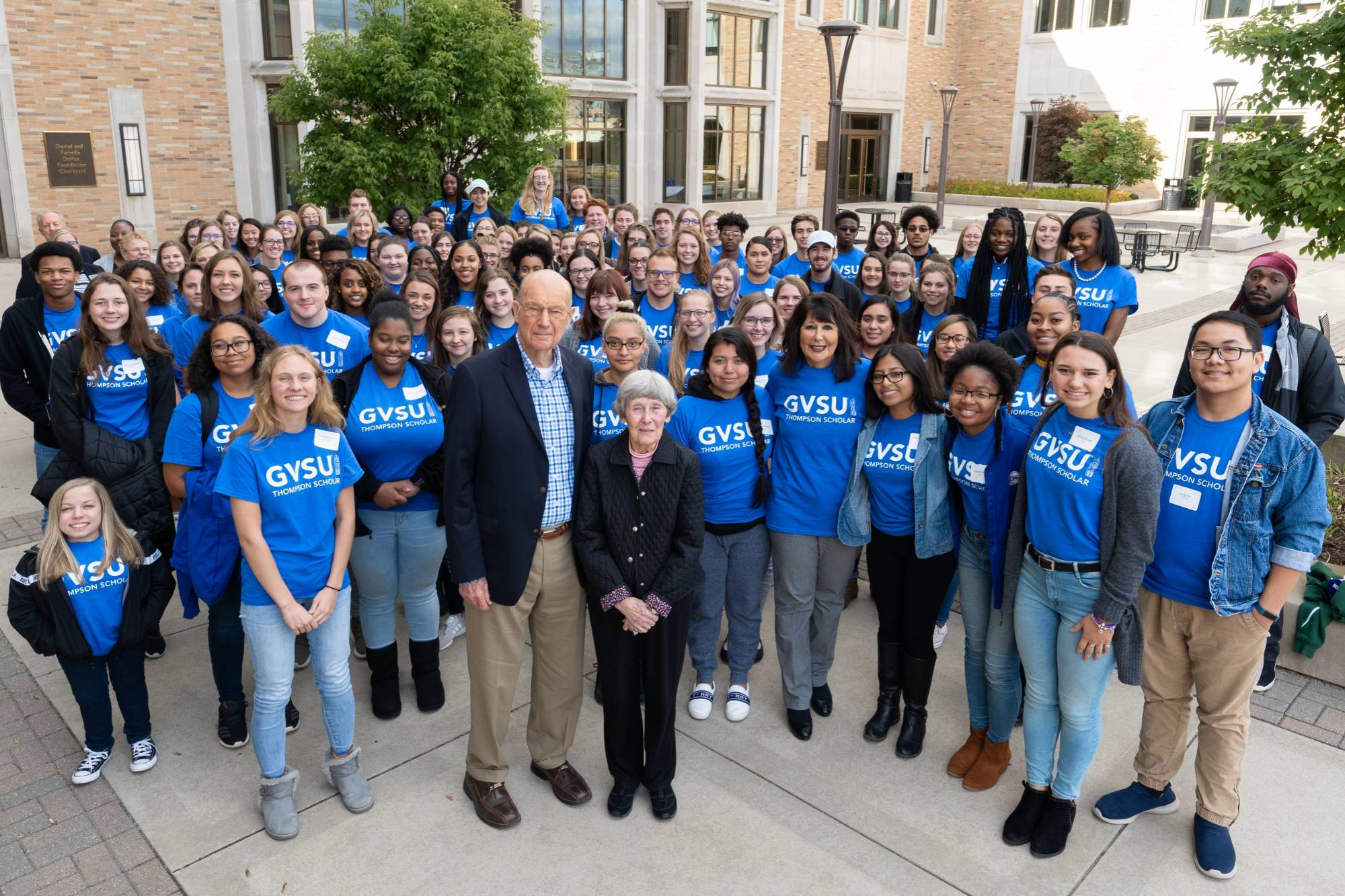 Bob and Ellen Thompson stand outside with President Mantella and a large group of students all wearing their blue Thompson Scholar t-shirts.